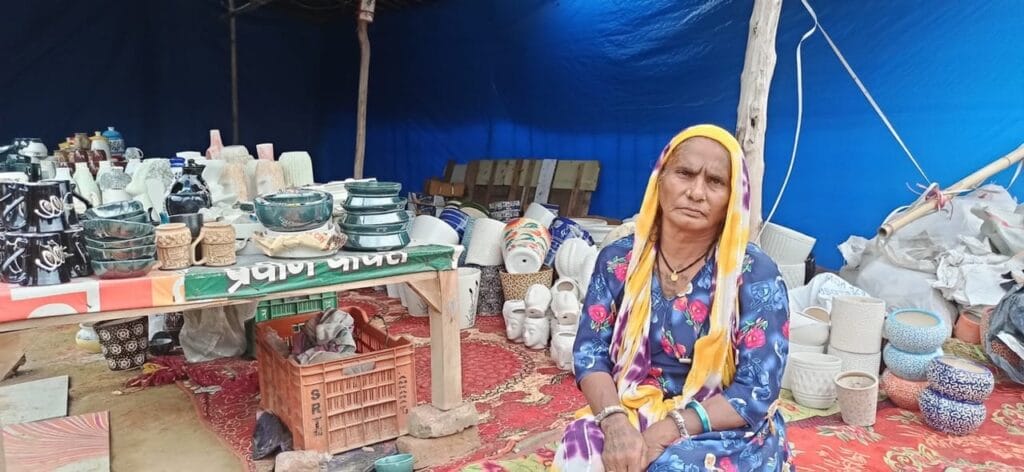 An elderly Banjara woman sits by her stall of handcrafted pottery.